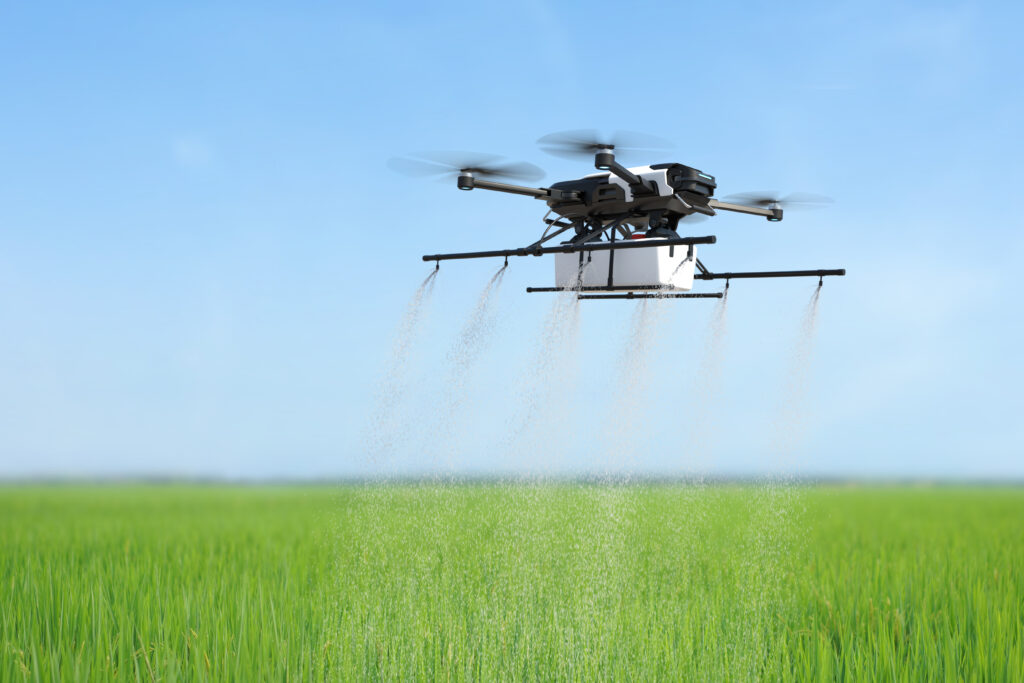 A drone can be seen carrying some equipment and spraying water on a farm field