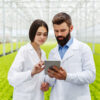A man and a woman scientist can be seen looking something on a tablet and behind them is a lush green hydroponic farm