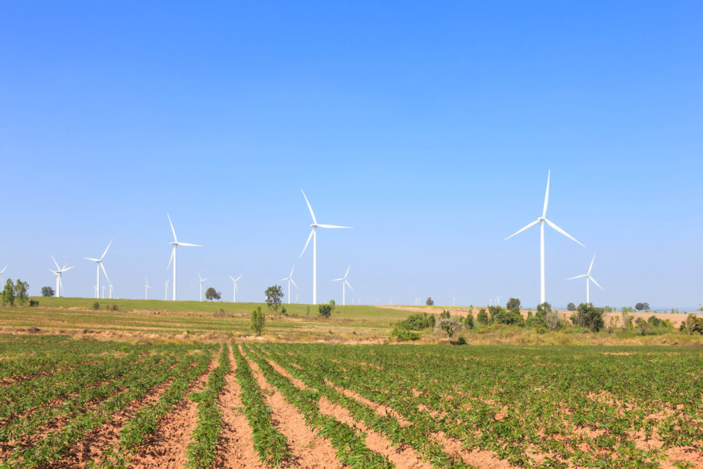 A chain of windmills can be seen in an open empty but green field with a clear blue sky surrounding it